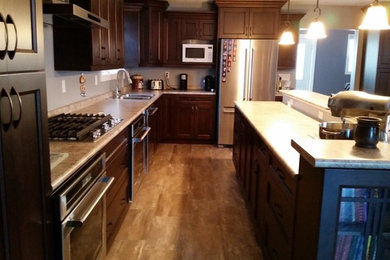 Example of a mid-sized classic l-shaped eat-in kitchen design in Calgary with a double-bowl sink, recessed-panel cabinets, dark wood cabinets, laminate countertops, stainless steel appliances and an island