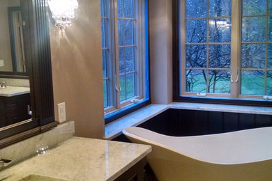 Example of a large master travertine floor bathroom design in Other with an undermount sink, recessed-panel cabinets, dark wood cabinets, marble countertops, a one-piece toilet and beige walls