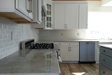 Eat-in kitchen - large coastal l-shaped eat-in kitchen idea in New York with a farmhouse sink, recessed-panel cabinets, white cabinets, gray backsplash, glass tile backsplash, stainless steel appliances and an island