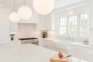 Photo of a mid-sized transitional l-shaped open plan kitchen in Boston with a farmhouse sink, shaker cabinets, white cabinets, quartz benchtops, white splashback, subway tile splashback, panelled appliances, medium hardwood floors, with island, white benchtop and brown floor.