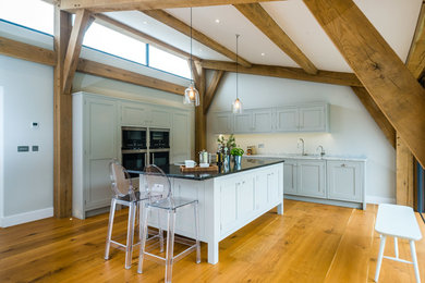Photo of a mid-sized country open plan kitchen in Wiltshire with shaker cabinets, grey cabinets, granite benchtops, stainless steel appliances, medium hardwood floors and with island.