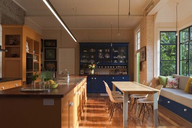 Design ideas for a mid-sized traditional single-wall kitchen in Sydney with flat-panel cabinets, light wood cabinets, solid surface benchtops, white splashback, ceramic splashback, stainless steel appliances, light hardwood floors and with island.