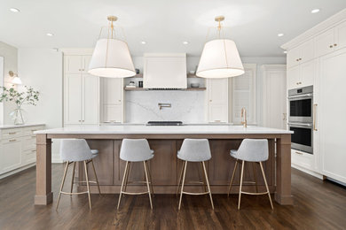 Inspiration for a large traditional u-shaped open plan kitchen in Calgary with a belfast sink, shaker cabinets, white cabinets, quartz worktops, white splashback, stone slab splashback, stainless steel appliances, medium hardwood flooring, an island, brown floors and white worktops.
