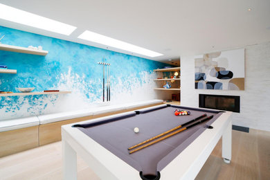 Large contemporary games room in Cornwall with blue walls, light hardwood flooring, a two-sided fireplace, a plastered fireplace surround, a wall mounted tv, beige floors and a feature wall.