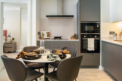 Design ideas for a medium sized modern grey and white l-shaped open plan kitchen in Manchester with a built-in sink, flat-panel cabinets, engineered stone countertops, white splashback, engineered quartz splashback, black appliances and black worktops.