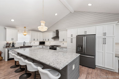 Photo of an expansive country l-shaped open plan kitchen in Chicago with a farmhouse sink, recessed-panel cabinets, white cabinets, granite benchtops, white splashback, subway tile splashback, stainless steel appliances, medium hardwood floors, with island, brown floor, white benchtop and vaulted.