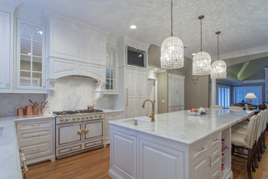 Example of a large classic u-shaped medium tone wood floor and brown floor enclosed kitchen design in Nashville with an undermount sink, white cabinets, marble countertops, white backsplash, paneled appliances, an island, raised-panel cabinets and marble backsplash