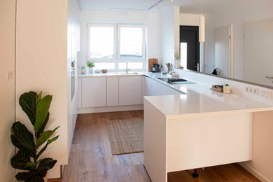 Offene, Mittelgroße Moderne Küche in U-Form mit Einbauwaschbecken, flächenbündigen Schrankfronten, weißen Schränken, Marmor-Arbeitsplatte, Küchenrückwand in Weiß, Rückwand aus Holz, weißen Elektrogeräten, braunem Holzboden, braunem Boden und weißer Arbeitsplatte in Frankfurt am Main