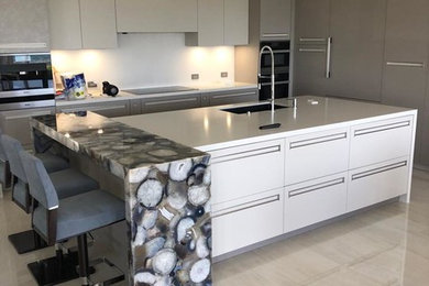 Kitchen - large modern slate floor kitchen idea in Miami with flat-panel cabinets, white cabinets, glass countertops, white backsplash, an island and white countertops