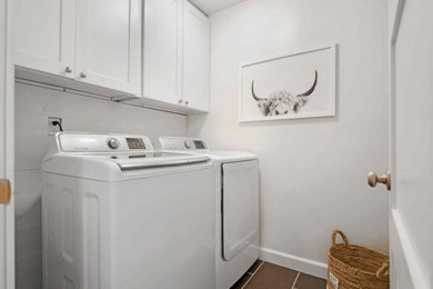 Ejemplo de cuarto de lavado lineal clásico de tamaño medio con armarios estilo shaker, puertas de armario blancas, paredes blancas, suelo de baldosas de cerámica, lavadora y secadora juntas y suelo marrón