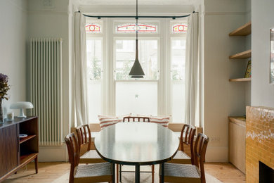 Design ideas for a medium sized contemporary open plan dining room in London with white walls, light hardwood flooring, a standard fireplace, a tiled fireplace surround, beige floors and a coffered ceiling.