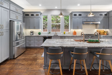 Example of a large transitional single-wall medium tone wood floor and brown floor eat-in kitchen design in Dallas with an undermount sink, shaker cabinets, gray cabinets, granite countertops, white backsplash, glass tile backsplash, stainless steel appliances, an island and gray countertops