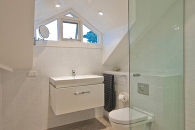 Photo of a contemporary bathroom in Sydney with flat-panel cabinets, white cabinets, a wall-mount toilet, white tile, porcelain tile, ceramic floors and an integrated sink.