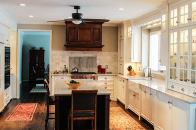 Photo of a traditional l-shaped eat-in kitchen in Detroit with white cabinets, beige splashback, stainless steel appliances, with island, a farmhouse sink, recessed-panel cabinets, dark hardwood floors and brown floor.