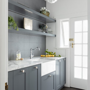 Foto di una piccola sala lavanderia classica con lavello stile country, ante in stile shaker, ante grigie, top in quarzite, paraspruzzi grigio, paraspruzzi con piastrelle in ceramica, pareti grigie, parquet scuro, lavatrice e asciugatrice nascoste, pavimento marrone, top multicolore, soffitto ribassato e boiserie