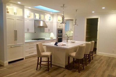 Mid-sized transitional single-wall open plan kitchen in Miami with shaker cabinets, white cabinets, panelled appliances, with island, a drop-in sink, granite benchtops, subway tile splashback, light hardwood floors, blue splashback and brown floor.