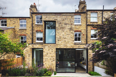 This is an example of a mid-sized traditional three-storey brick townhouse exterior in London with a flat roof.