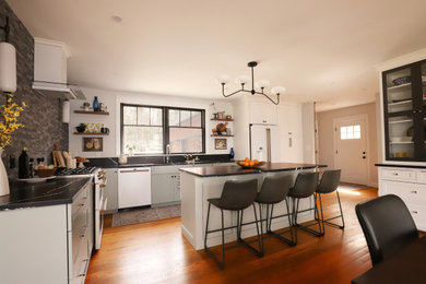 Photo of a large transitional l-shaped eat-in kitchen in Portland Maine with a single-bowl sink, shaker cabinets, green cabinets, quartz benchtops, grey splashback, stone tile splashback, white appliances, medium hardwood floors, with island and black benchtop.