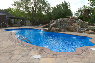 Large traditional backyard custom-shaped natural pool in Other with a water feature and natural stone pavers.