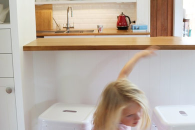 Modelo de cocina marinera con armarios estilo shaker, puertas de armario blancas, encimera de madera, salpicadero blanco, salpicadero de azulejos tipo metro y suelo de madera en tonos medios
