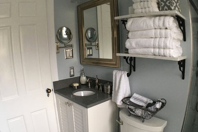 Small transitional white tile and ceramic tile gray floor bathroom photo in Detroit with louvered cabinets, white cabinets, a two-piece toilet, blue walls, an undermount sink, solid surface countertops and a hinged shower door