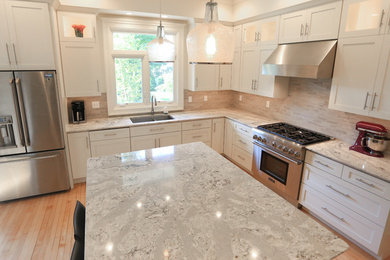 Inspiration for a mid-sized transitional l-shaped light wood floor enclosed kitchen remodel in Other with an undermount sink, recessed-panel cabinets, white cabinets, gray backsplash, ceramic backsplash, stainless steel appliances, an island and granite countertops