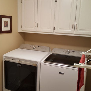 カンザスシティの小さいトラディショナルスタイルのおしゃれな洗濯室 (レイズドパネル扉のキャビネット、白いキャビネット、ベージュの壁、カーペット敷き、左右配置の洗濯機・乾燥機) の写真
