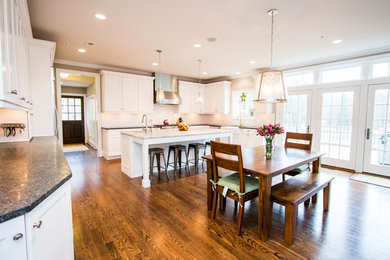 Inspiration for a large transitional l-shaped dark wood floor open concept kitchen remodel in Philadelphia with a farmhouse sink, recessed-panel cabinets, white cabinets, granite countertops, white backsplash, subway tile backsplash, stainless steel appliances and an island