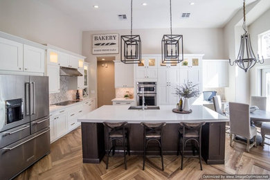 Eat-in kitchen - large traditional l-shaped light wood floor and brown floor eat-in kitchen idea in Phoenix with a farmhouse sink, shaker cabinets, white cabinets, quartzite countertops, gray backsplash, matchstick tile backsplash, stainless steel appliances and an island