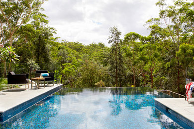 Ejemplo de piscina infinita moderna de tamaño medio a medida en patio trasero con suelo de baldosas