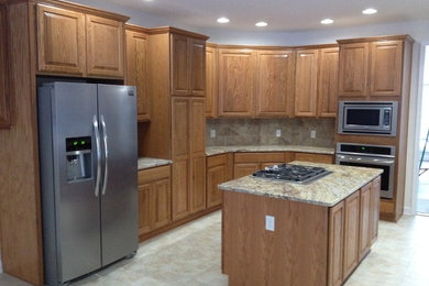 Inspiration for a mid-sized timeless l-shaped travertine floor eat-in kitchen remodel in Other with raised-panel cabinets, medium tone wood cabinets, granite countertops, beige backsplash, ceramic backsplash, stainless steel appliances, an island and a double-bowl sink