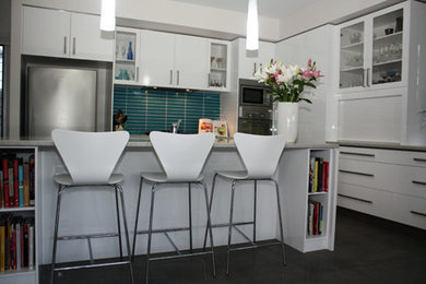 Inspiration for a mid-sized contemporary l-shaped eat-in kitchen in Sunshine Coast with flat-panel cabinets, white cabinets, granite benchtops, green splashback, ceramic splashback, stainless steel appliances, with island and black floor.