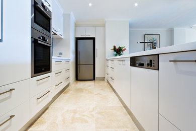 Photo of a small modern galley kitchen in Sydney with flat-panel cabinets, white cabinets, quartz benchtops, multi-coloured splashback, glass tile splashback, stainless steel appliances, a double-bowl sink and travertine floors.