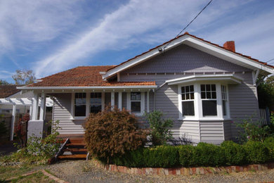 Design ideas for a mid-sized traditional one-storey grey house exterior in Melbourne with wood siding, a gable roof, a tile roof, a red roof and board and batten siding.