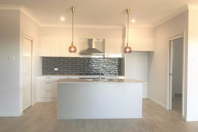 Inspiration for a mid-sized modern galley kitchen in Newcastle - Maitland with a double-bowl sink, white cabinets, quartzite benchtops, grey splashback, subway tile splashback, stainless steel appliances, with island and beige floor.