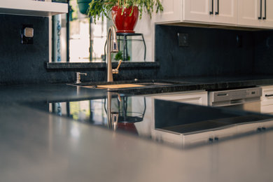 Example of a large minimalist l-shaped medium tone wood floor and brown floor eat-in kitchen design in Phoenix with a single-bowl sink, shaker cabinets, white cabinets, granite countertops, black backsplash, granite backsplash, stainless steel appliances, a peninsula and black countertops