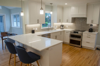 This is an example of a large contemporary l-shaped kitchen/diner in Minneapolis with a submerged sink, flat-panel cabinets, white cabinets, granite worktops, grey splashback, metro tiled splashback, stainless steel appliances, dark hardwood flooring, a breakfast bar, brown floors and white worktops.