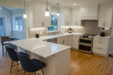 Idée de décoration pour une grande cuisine américaine design en L avec un évier encastré, un placard à porte plane, des portes de placard blanches, un plan de travail en granite, une crédence grise, une crédence en carrelage métro, un électroménager en acier inoxydable, parquet foncé, une péninsule, un sol marron et un plan de travail blanc.