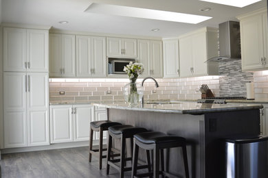 Large minimalist l-shaped laminate floor and multicolored floor kitchen photo in Sacramento with a double-bowl sink, beaded inset cabinets, beige cabinets, granite countertops, white backsplash, glass tile backsplash, stainless steel appliances, an island and multicolored countertops