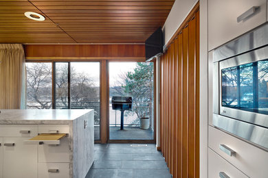 Mid-sized trendy single-wall slate floor eat-in kitchen photo in Minneapolis with an undermount sink, flat-panel cabinets, white cabinets, marble countertops, white backsplash, glass sheet backsplash, stainless steel appliances and an island