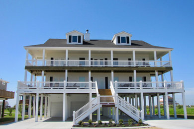 This is an example of a large beach style two-storey white house exterior in Houston with vinyl siding and a shingle roof.