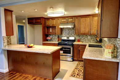 Mid-sized traditional l-shaped kitchen in Los Angeles with an undermount sink, raised-panel cabinets, medium wood cabinets, brown splashback, mosaic tile splashback, stainless steel appliances, porcelain floors, with island, granite benchtops and beige floor.