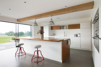 Contemporary galley kitchen in Other with flat-panel cabinets, white cabinets, wood benchtops, white splashback, concrete floors and with island.
