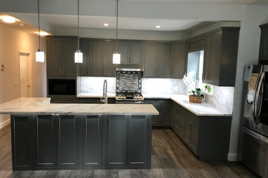 Inspiration for a mid-sized timeless l-shaped light wood floor and gray floor eat-in kitchen remodel in Other with a farmhouse sink, recessed-panel cabinets, gray cabinets, marble countertops, white backsplash, marble backsplash, stainless steel appliances, an island and white countertops