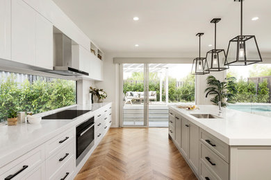 Photo of a large modern galley eat-in kitchen in Melbourne with an undermount sink, shaker cabinets, white cabinets, quartz benchtops, white splashback, stone slab splashback, black appliances, light hardwood floors, with island, brown floor and white benchtop.