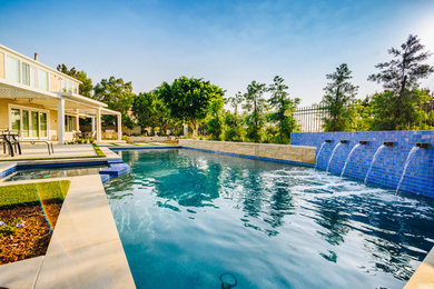Photo of a large contemporary backyard rectangular lap pool in Orange County with a water feature and natural stone pavers.