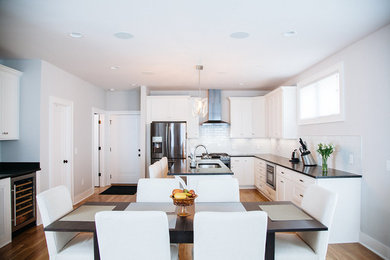 Trendy u-shaped light wood floor kitchen photo in Nashville with an undermount sink, recessed-panel cabinets, white cabinets, white backsplash, subway tile backsplash, stainless steel appliances and an island