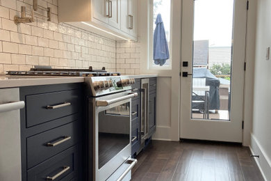 Example of a mid-sized classic single-wall medium tone wood floor and brown floor eat-in kitchen design in Seattle with a farmhouse sink, quartz countertops, white backsplash, ceramic backsplash, stainless steel appliances, white countertops, shaker cabinets, black cabinets and no island