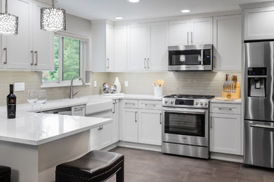 Mid-sized transitional u-shaped eat-in kitchen in Seattle with a farmhouse sink, shaker cabinets, white cabinets, quartz benchtops, grey splashback, glass tile splashback, stainless steel appliances, porcelain floors, a peninsula, grey floor and white benchtop.