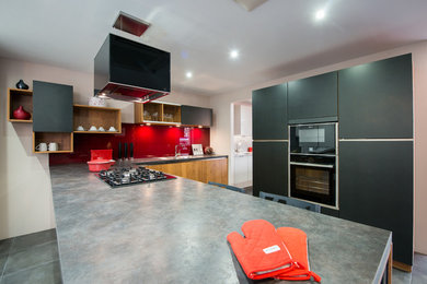 This is an example of a contemporary l-shaped open plan kitchen in London with a double-bowl sink, flat-panel cabinets, black cabinets, laminate benchtops, red splashback, glass sheet splashback and black appliances.